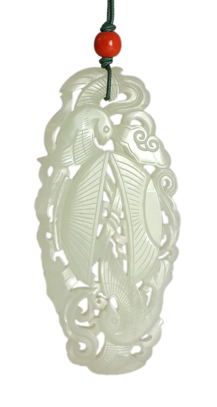 A Chinese white jade twin phoenix reticulated plaque, 19th century, 8.7cm, suspended from a wood stand with coral bead to the cord